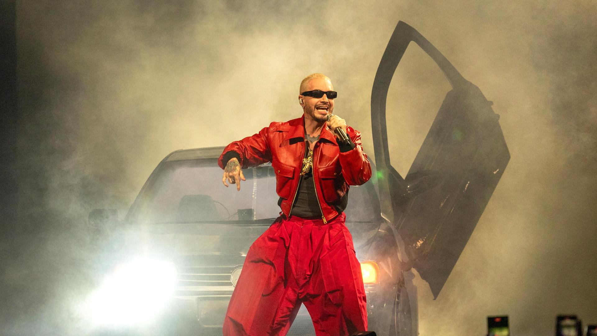 Der Sänger J Balvin steht in rotem Outfit vor einem Auto und singt, die Bühne ist mit Kunstnebel verhangen Der Sänger J Balvin steht in rotem Outfit vor einem Auto und singt, die Bühne ist mit Kunstnebel verhangen