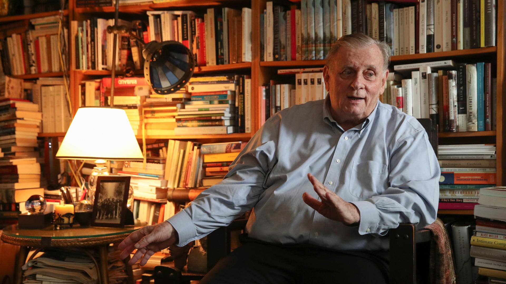 Edmund White sitzt auf einem Stuhl in seiner Wohnung, im Hintergrund ein riesiges Bücherregal Edmund White sitzt auf einem Stuhl in seiner Wohnung, im Hintergrund ein riesiges Bücherregal