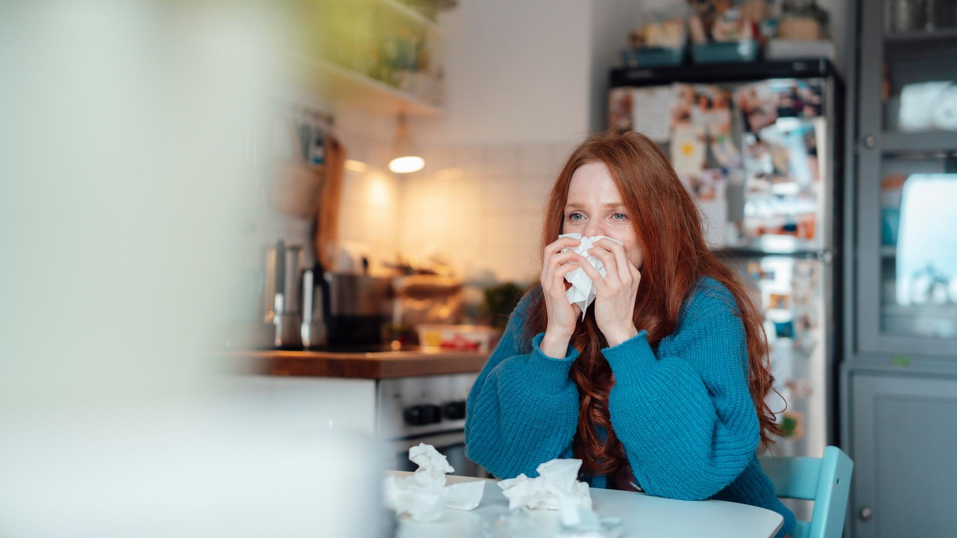Eine Frau sitzt krank in ihrer Küche am Küchentisch