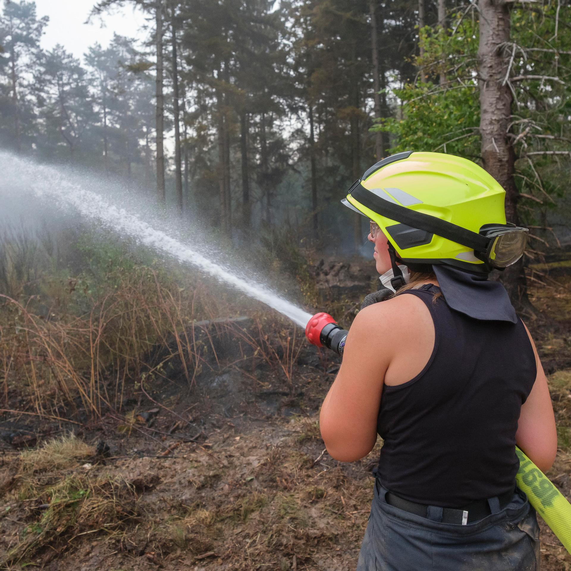 Eine Feuerwehrfrau löscht eine verbrannte Wald-Fläche.