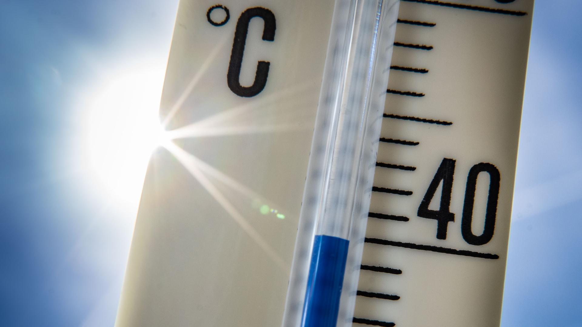 Ein Außenthermometer zeigt vor dem blauen Himmel und der Sonne eine Temperatur von nahezu 40 Grad Celsius an. 