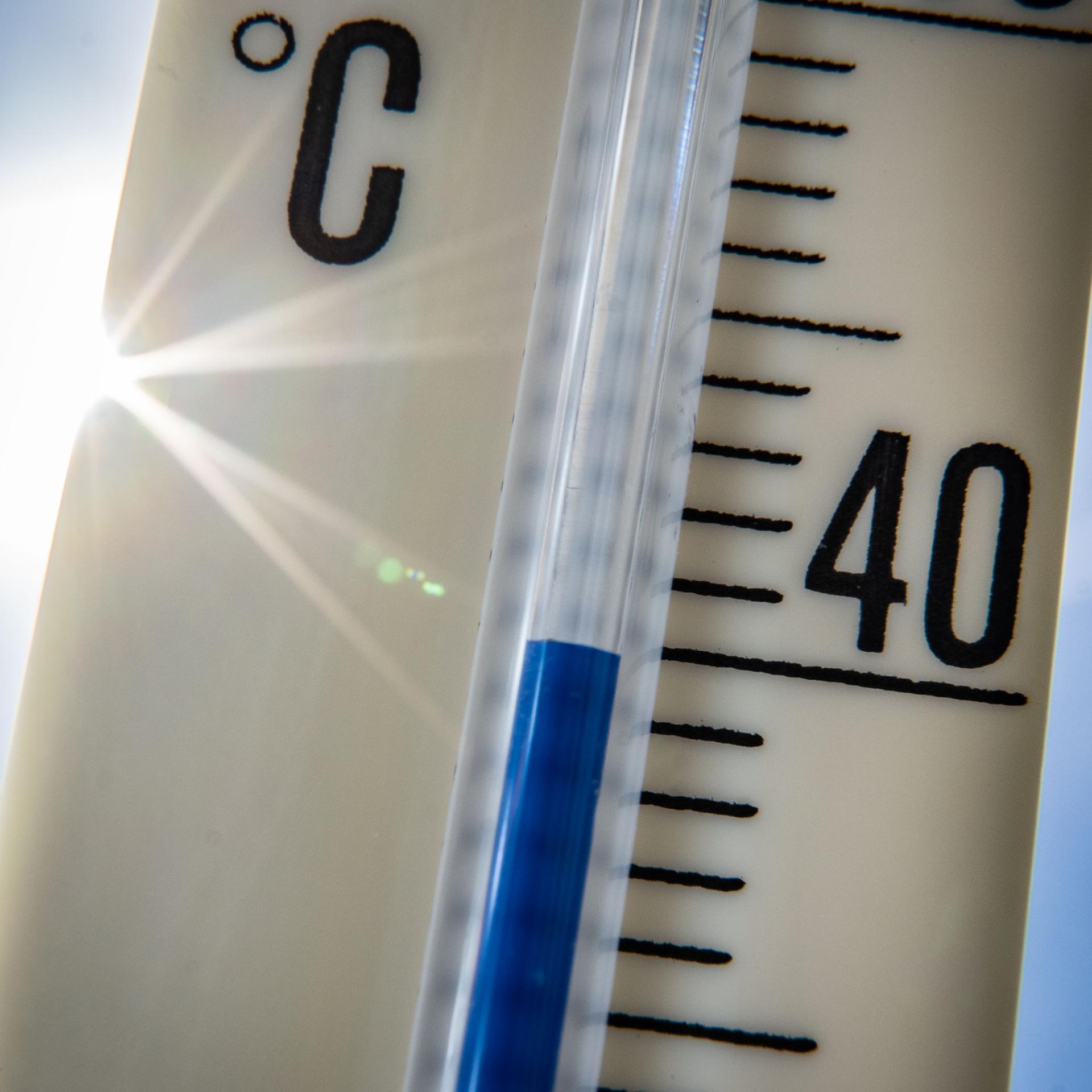 Ein Außenthermometer zeigt vor dem blauen Himmel und der Sonne eine Temperatur von nahezu 40 Grad Celsius an. 