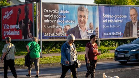 Fußgänger überqueren eine Straße vor Wahlplakaten in Zagreb, Kroatien.