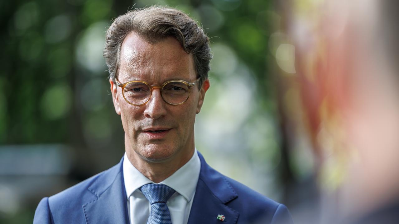 Ministerpräsident Hendrik Wüst steht im Freien, im Hintergrund Bäume. Er trägt einen hellblauen Sakko mit NRW-Anstecker am Revers und eine hellbraune Brille. Ministerpräsident Hendrik Wüst steht im Freien, im Hintergrund Bäume. Er trägt einen hellblauen Sakko mit NRW-Anstecker am Revers und eine hellbraune Brille.
