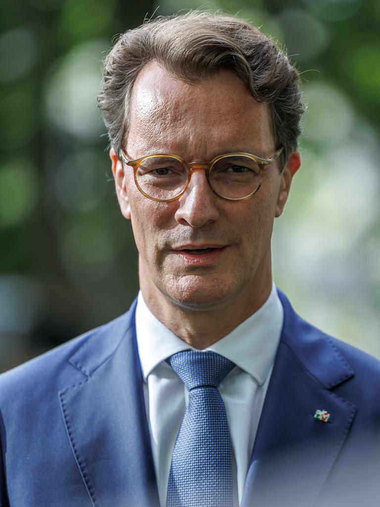 Ministerpräsident Hendrik Wüst steht im Freien, im Hintergrund Bäume. Er trägt einen hellblauen Sakko mit NRW-Anstecker am Revers und eine hellbraune Brille. Ministerpräsident Hendrik Wüst steht im Freien, im Hintergrund Bäume. Er trägt einen hellblauen Sakko mit NRW-Anstecker am Revers und eine hellbraune Brille.