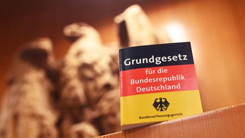 Vor einem steinernen Bundesadler steht eine Miniatur-Ausgabe des Grundgesetzes auf einem Schreibtisch.