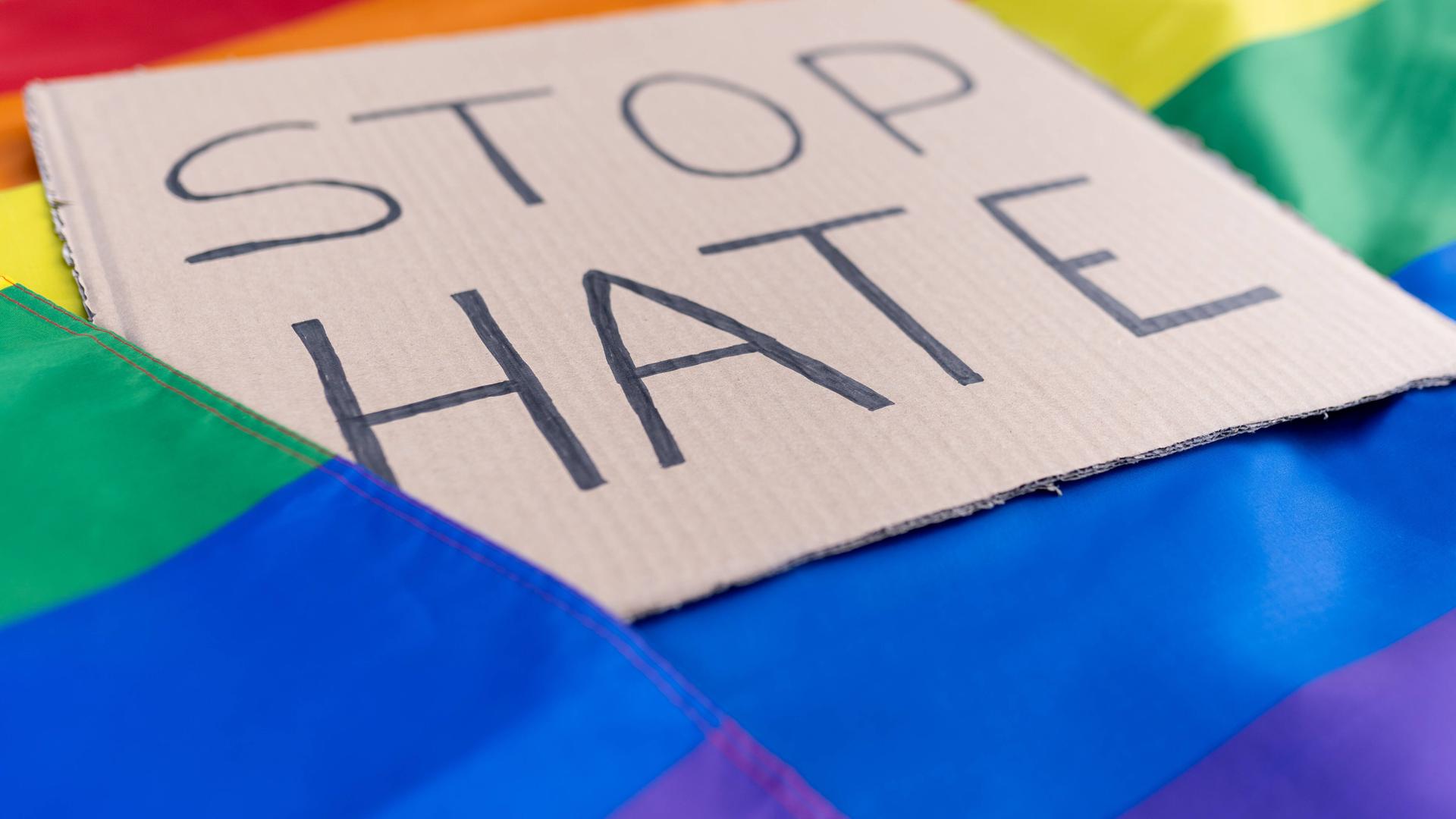 Top view full body carton with Stop Hate inscription placed on colorful rainbow LGBT flag on light street in city Miguel