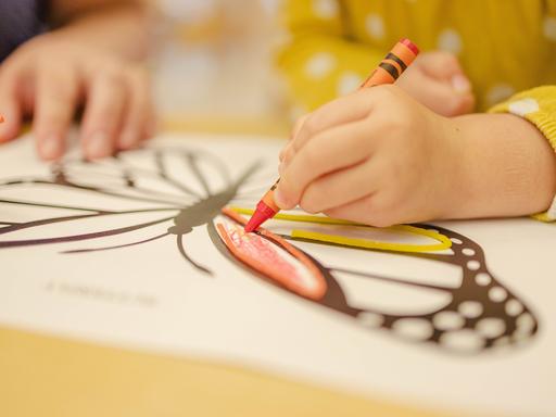 Ein Kind malt mit einem roten Wachsmalstift einen Schmetterling aus.