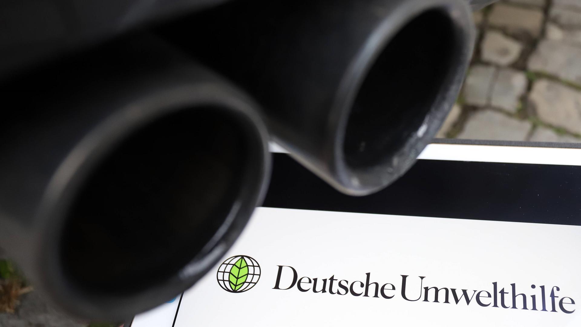 Auspuffrohre eines Fahrzeugs, darunter ein iPad mit Schriftzug und Logo der Deutschen Umwelthilfe
