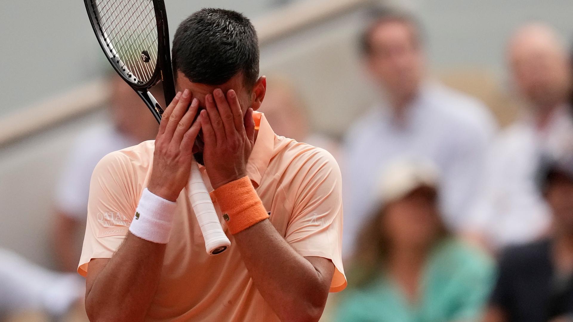 Novak Djokovic scheidet bei den French Open in Paris aus und hält sich die Hände vors Gesicht. 
