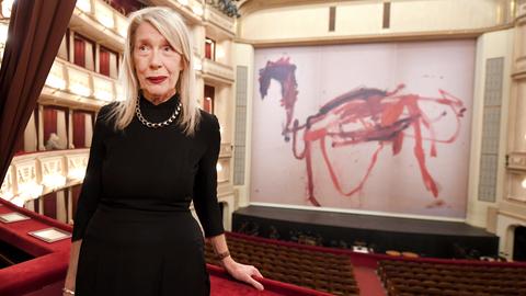Die Künstlerin Martha Jungwirth steht in einem Opernhaus, das mit einem Vorhang mit ihrer Malerei geschmuückt ist.