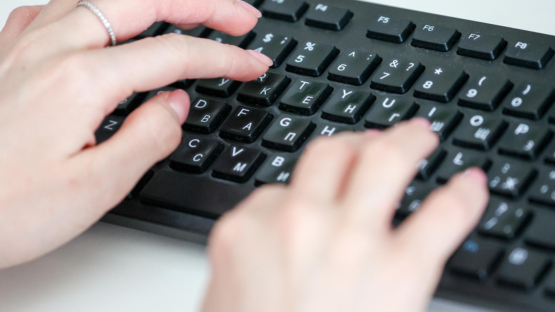 Hände tippen auf einer Computertastatur mit kyrillischen Buchstaben.