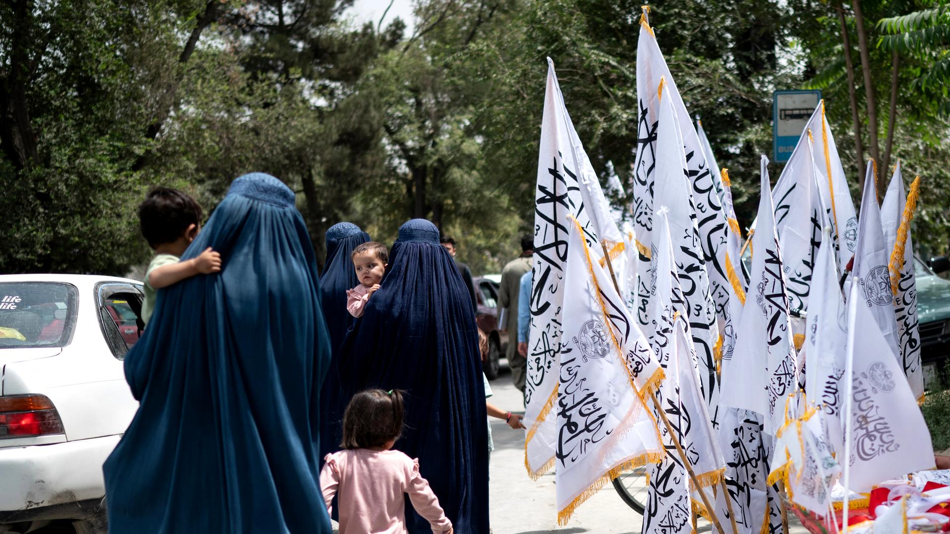 Afghanische Frauen in Burkas gehen am Vorabend des vierten Jahrestags der Machtübernahme der Taliban im Jahr 2021 an Taliban-Flaggen vorbei, in Kabul am 14. August 2025. (Foto: Wakil Kohsar / AFP)