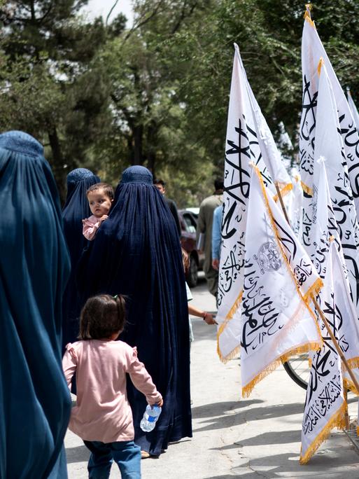 Afghanische Frauen in Burkas gehen am Vorabend des vierten Jahrestags der Machtübernahme der Taliban im Jahr 2021 an Taliban-Flaggen vorbei, in Kabul am 14. August 2025. (Foto: Wakil Kohsar / AFP)