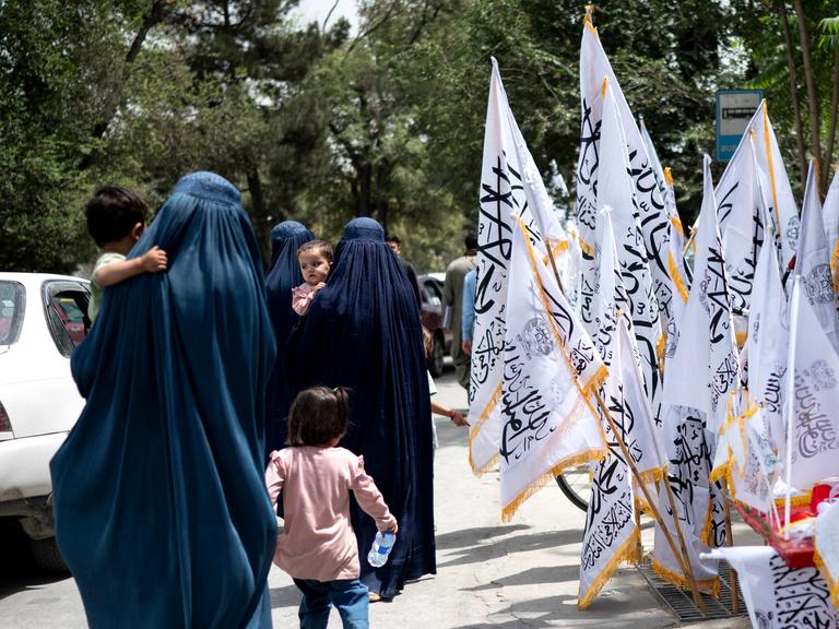 Afghanische Frauen in Burkas gehen am Vorabend des vierten Jahrestags der Machtübernahme der Taliban im Jahr 2021 an Taliban-Flaggen vorbei, in Kabul am 14. August 2025. (Foto: Wakil Kohsar / AFP)
