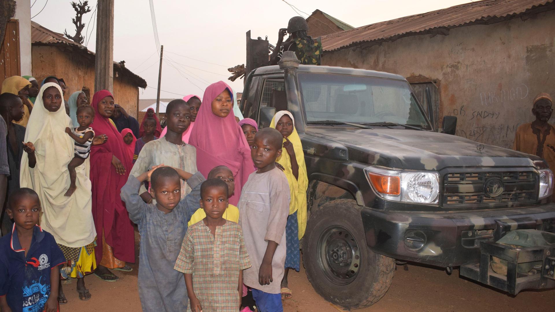 Ein Fahrzeug nigerianischer Sicherheitskräfte wird nach der Entführung von rund 300 Schülerinnen und Schülern von Frauen und Kindern flankiert.