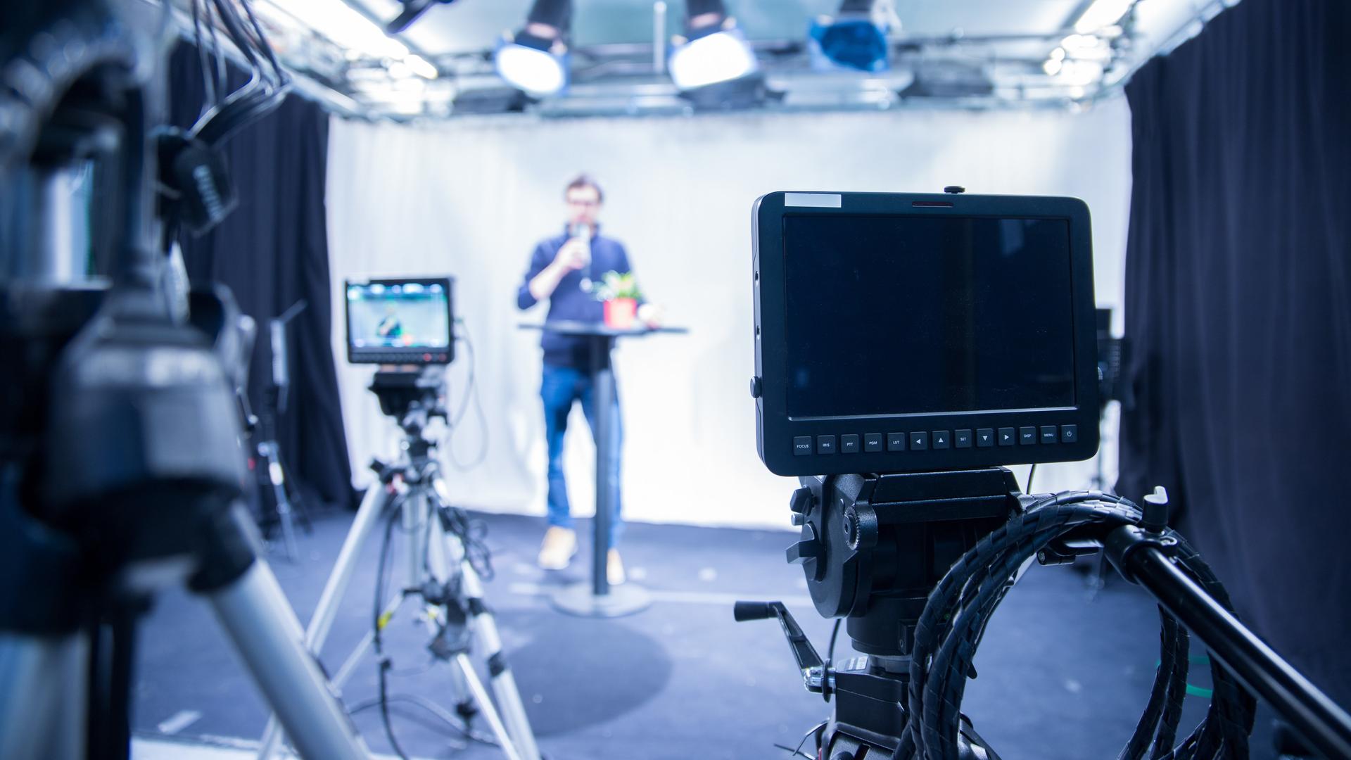 Ein Mann steht vor Kameras und hält einen Vortrag. Ein Mann steht vor Kameras und hält einen Vortrag.