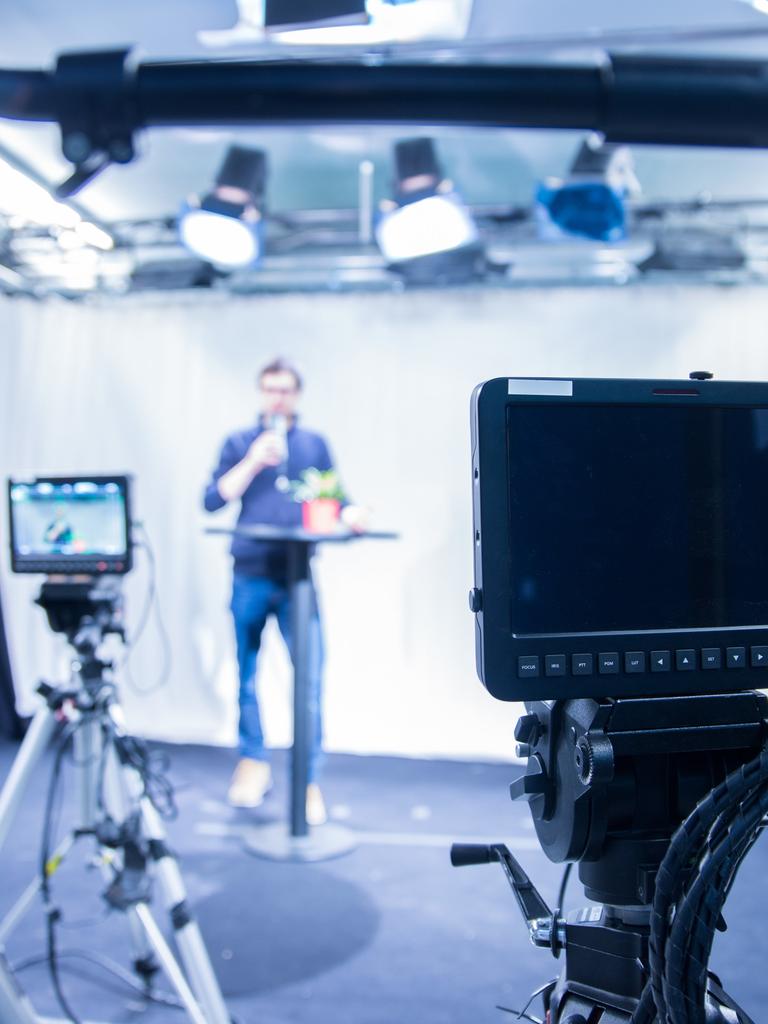 Ein Mann steht vor Kameras und hält einen Vortrag.