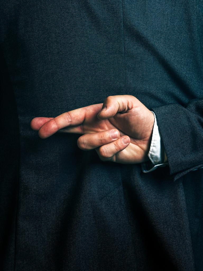 Eine Person im Anzug hält hinter dem Rücken die Finger einer Hand überkreuzt.