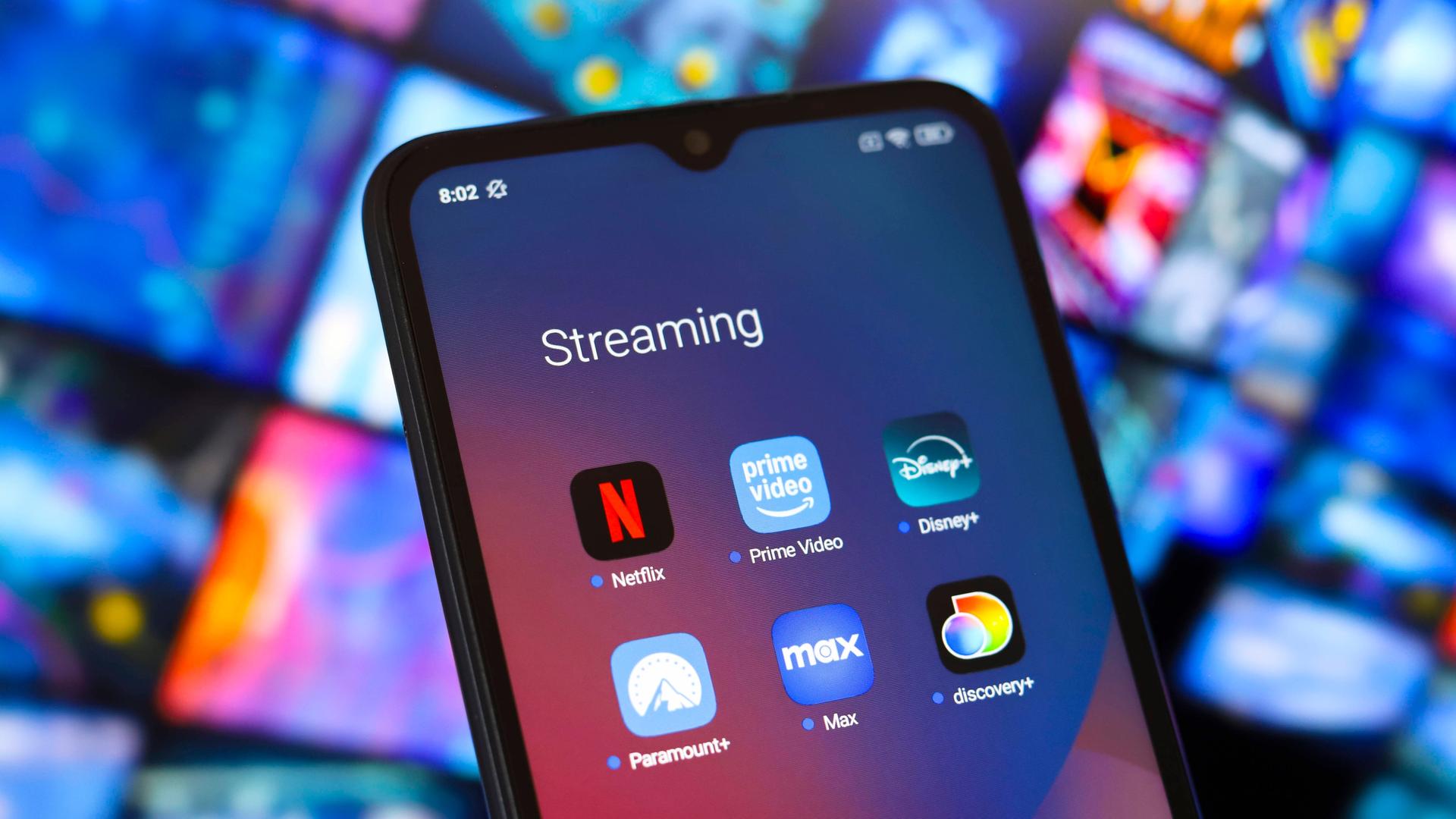 Ein Smartphone mit den Apps der Streaming-Anbieter Amazon, Disney und Netflix vor dem Hintergrund anderer verschwommener Bildschirme