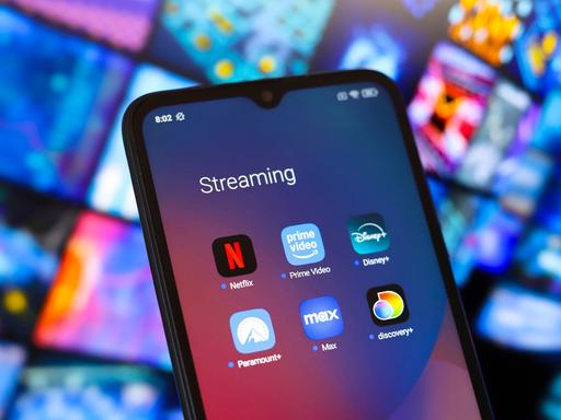 Ein Smartphone mit den Apps der Streaming-Anbieter Amazon, Disney und Netflix vor dem Hintergrund anderer verschwommener Bildschirme