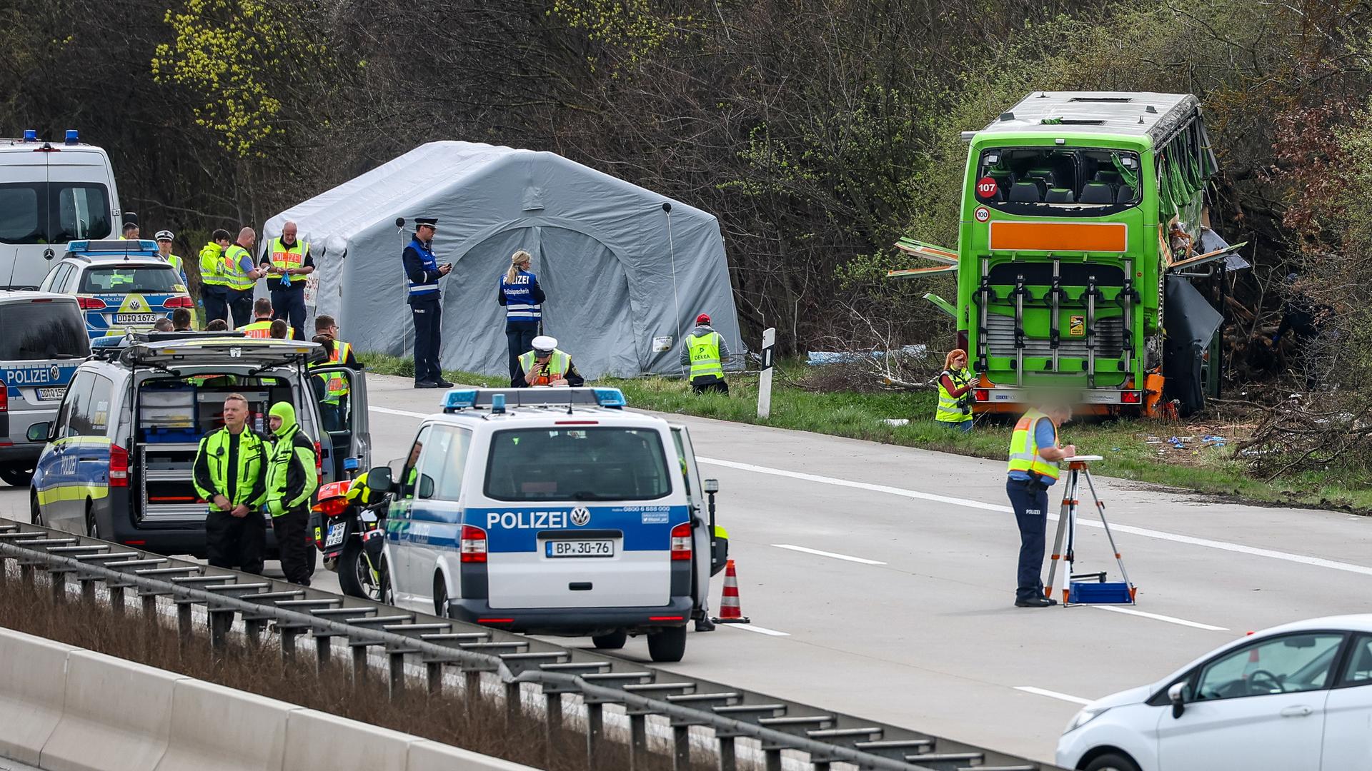 Der verunglückte Bus steht am Straßenrand; daneben ein weißes Zelt. Auf der Autobahn Polizeifahrzeuege und Polizisten.