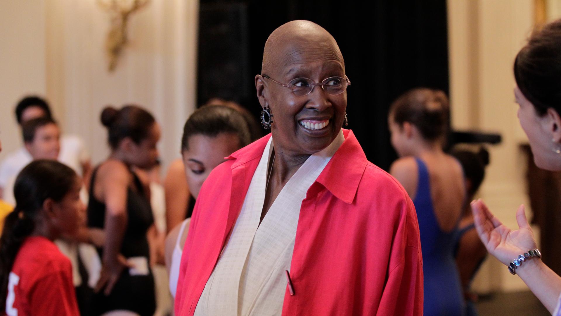 Die Tänzerin und Choreographin Judith Jamison steht lächelnd inmitten von Tänzerinnen. Die Tänzerin und Choreographin Judith Jamison steht lächelnd inmitten von Tänzerinnen.