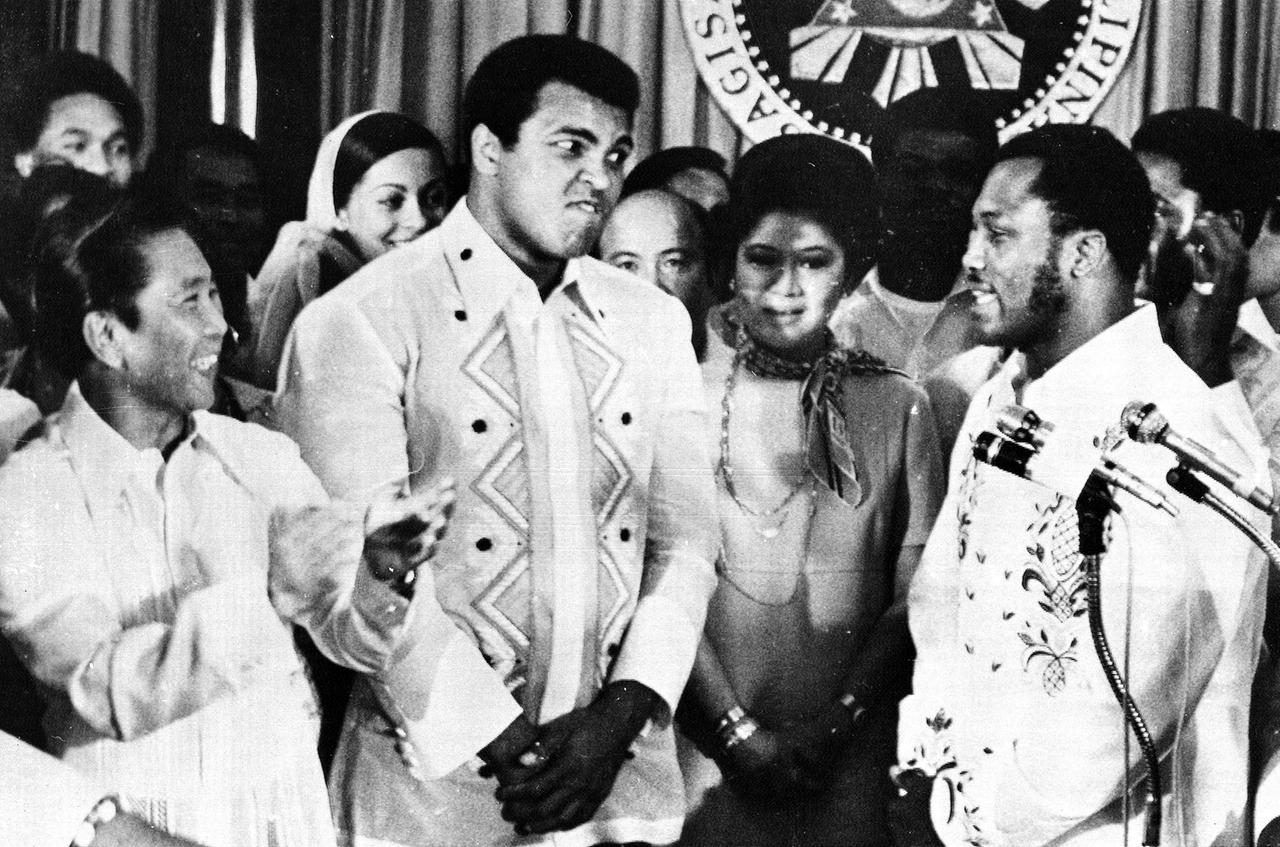 Philippines President Ferdinand Marcos, left, applauds as challenger Joe Frazier, right, makes some remarks about world champion Muhammad Ali, second from left, during their call on Marcos at the Malacanang Palace in Manila, Philippines, on Sept. 18, 1975. Between the two fighters is Marco's wife Imelda. (AP Photo/Jess Tan)