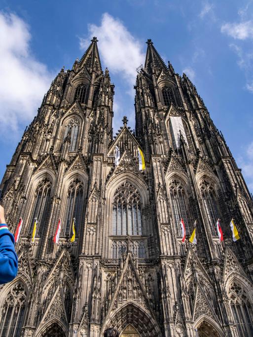 Zwei Personen stehen vor dem Kölner Dom. Sie sind von hinten zu sehen. Eine Person fotografiert den Kölner Dom.
