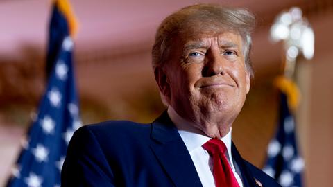 Ex-US-Präsident Trump verzieht während einer Rede das Gesicht. Im Hintergrund zwei Flaggen der Vereinigten Staaten.