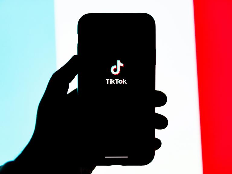 Silhouette einer Hand, die ein Smartphone mit einem TikTok-Logo auf dem Screen, hält