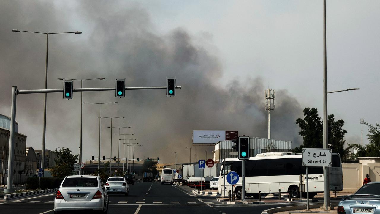 Autos fahren in Doha auf einer Straße, im Hintergrund sieht man Rauch aufsteigen.