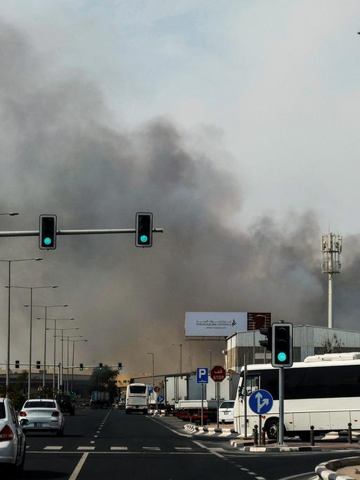 Autos fahren in Doha auf einer Straße, im Hintergrund sieht man Rauch aufsteigen.