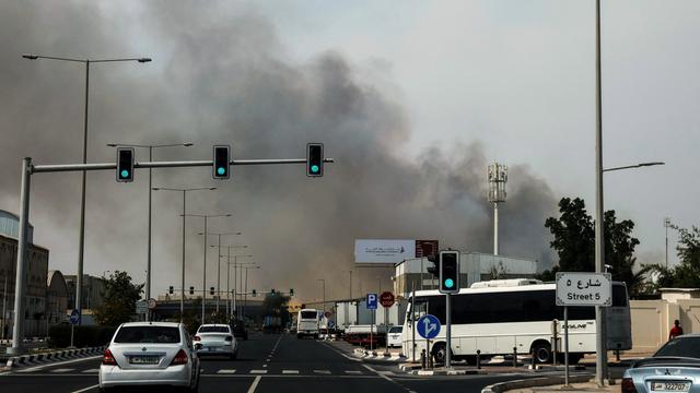 Autos fahren in Doha auf einer Straße, im Hintergrund sieht man Rauch aufsteigen.