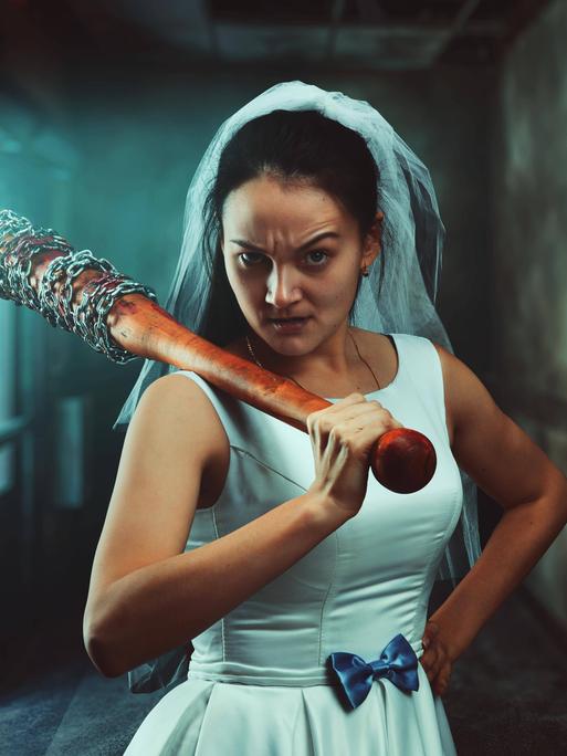 Eine Braut in weißem Hochzeitskleid mit Baseballschläger.