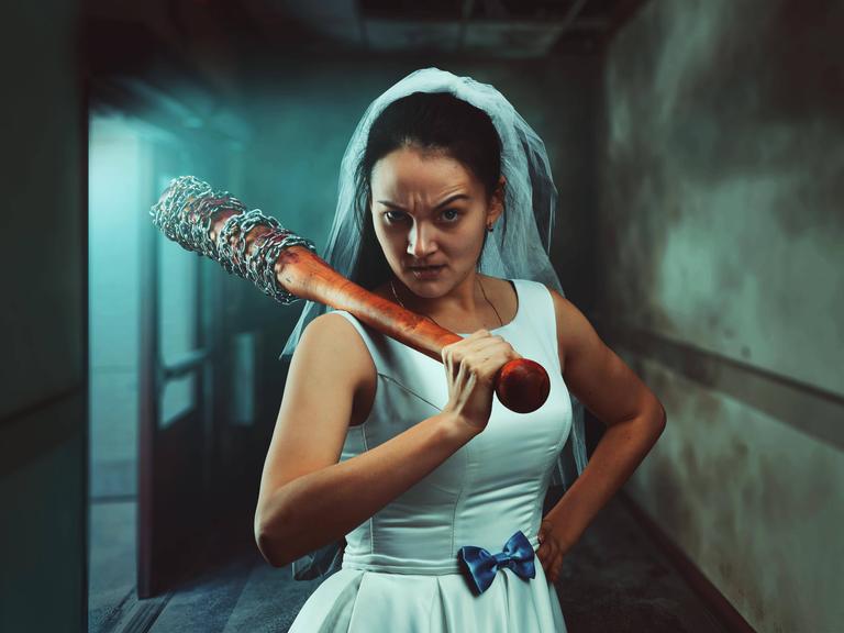 Eine Braut in weißem Hochzeitskleid mit Baseballschläger.