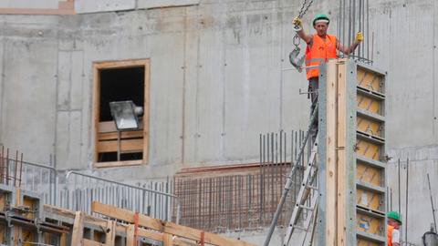 Zwei Bauarbeiter in orangen Westen stehen auf einer Großbaustelle
