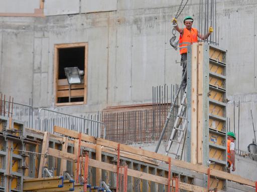 Zwei Bauarbeiter in orangen Westen stehen auf einer Großbaustelle