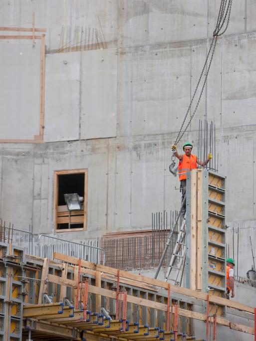 Zwei Bauarbeiter in orangen Westen stehen auf einer Großbaustelle