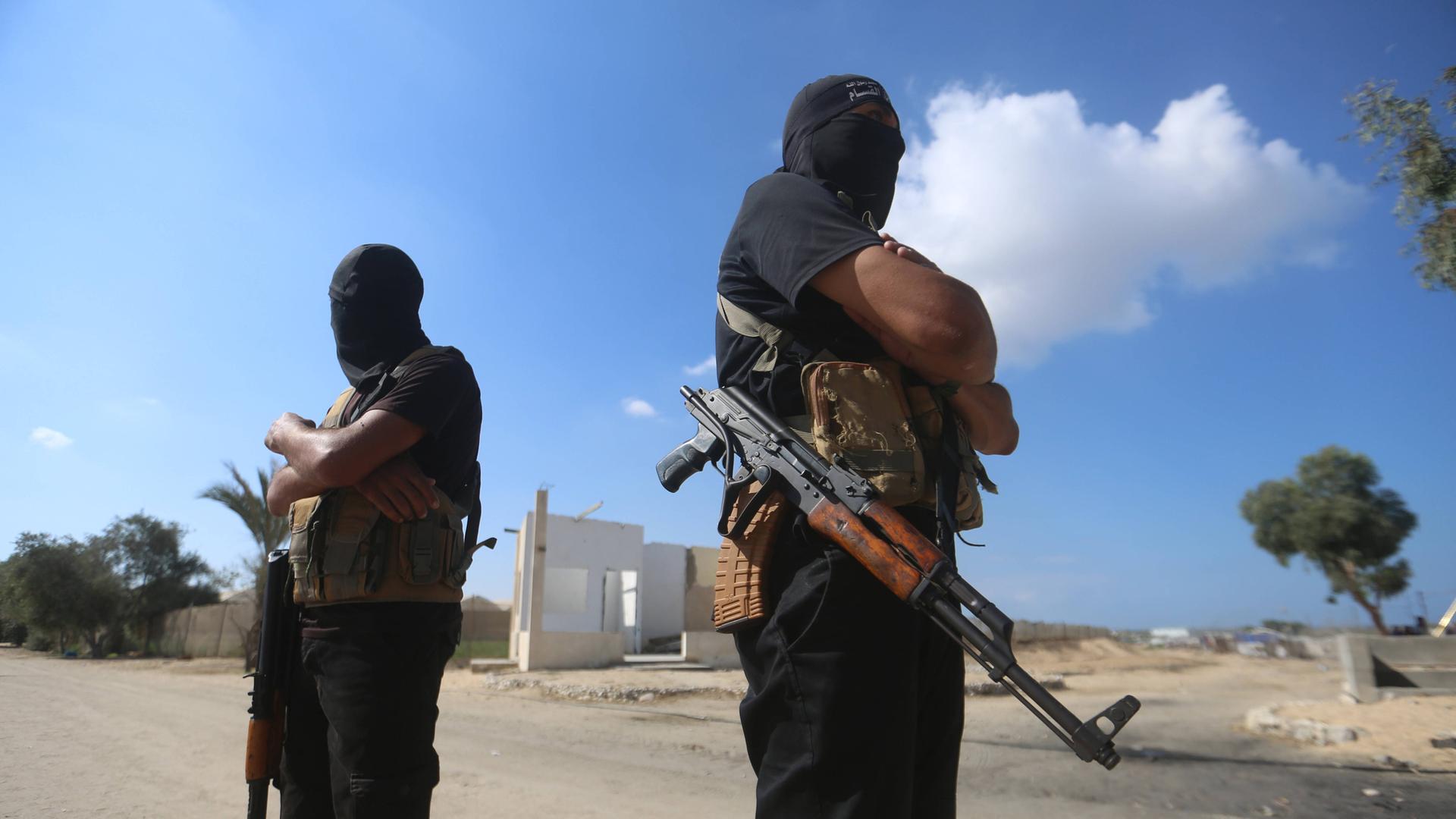 Militante Palästinenser der Ezzedine al-Qassam-Brigaden, dem militärischen Flügel der Hamas, stehen mit Waffen und überkreuzten Armen auf einer Straße. Ihre Köpfe sind vermummt.