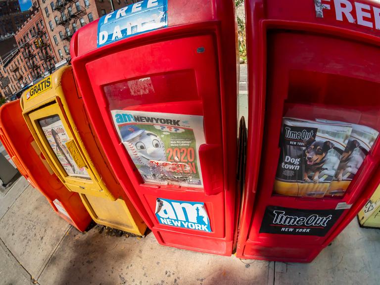Vier Kästen in rot und gelb an einer Straße in New York, aus denen sich Passanten Gratiszeitungen nehmen können