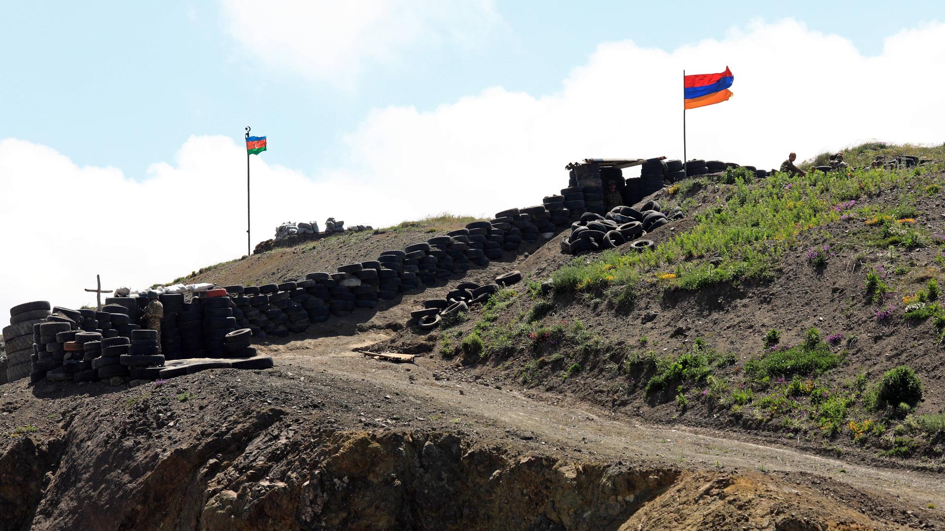 Ein armenischer Militärposten, über den Befestigungen weht die armenische Fahne, Reifenstapel sind zum Schutz aufgestellt, im Hintergrund weht die aserbaidschanische Fahne an einem anderen Militärposten.