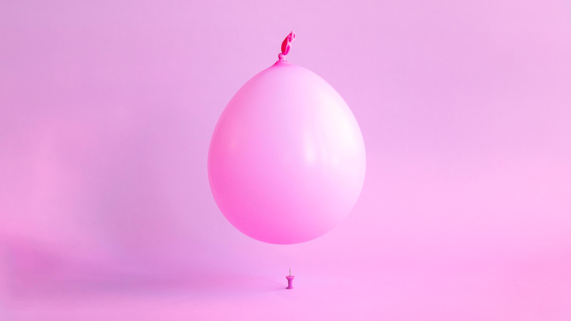 Ein rosa Ballon schwebt über einer Reißzwecke. Ein rosa Ballon schwebt über einer Reißzwecke.