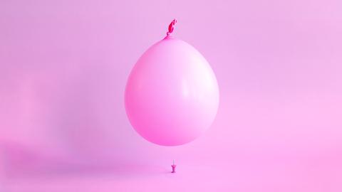 Ein rosa Ballon schwebt über einer Reißzwecke.