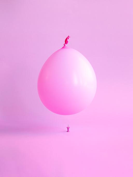 Ein rosa Ballon schwebt über einer Reißzwecke.