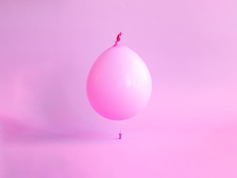 Ein rosa Ballon schwebt über einer Reißzwecke.