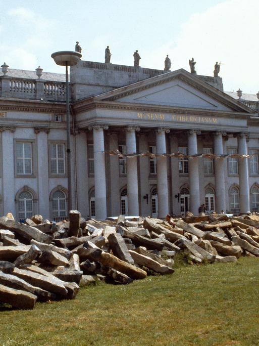Zum  Start der" documenta 7" ließ Joseph Beuys 7.000 Basaltstelen alsDreieck auf dem Friedrichsplatz in Kassel aufhäufen. An dessen Spitze pflanzte er die erste von 7.000 Eichen
