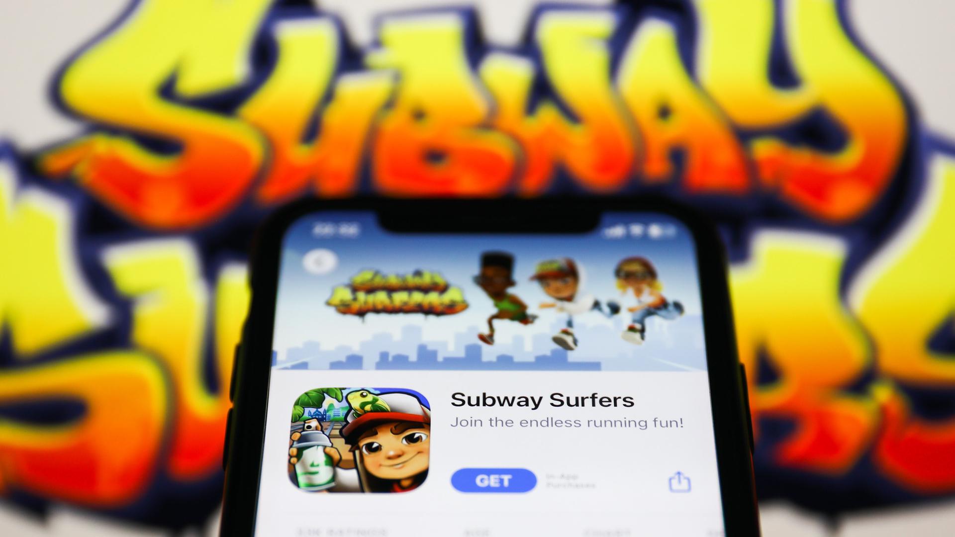 Ein Handy zeigt die App "Subway Surfers" im Hintergrund ist der Schriftzug des Spiels zu sehen. Ein Handy zeigt die App "Subway Surfers" im Hintergrund ist der Schriftzug des Spiels zu sehen.