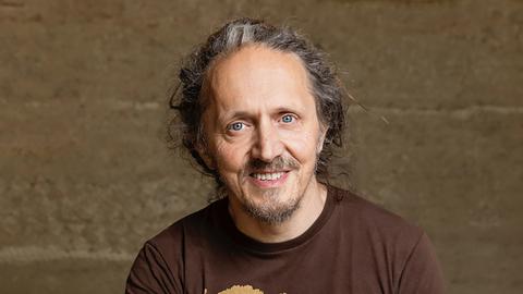 Harry Putz trägt ein braunes´T-Shirt mit der Aufschrift "Positive Intellectual Person" und schaut freundlich in die Kamera.