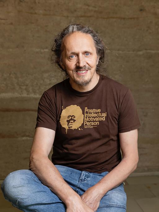 Harry Putz trägt ein braunes´T-Shirt mit der Aufschrift "Positive Intellectual Person" und schaut freundlich in die Kamera.